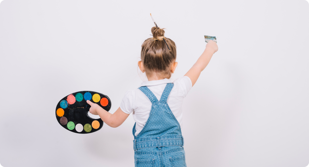 bambina con pennello e tempere colorate in mano mentre
sta per dipingere un muro bianco